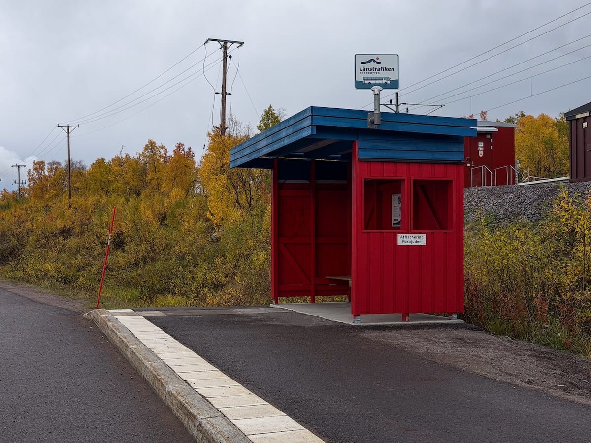 a red bus stop on a highway during autumn