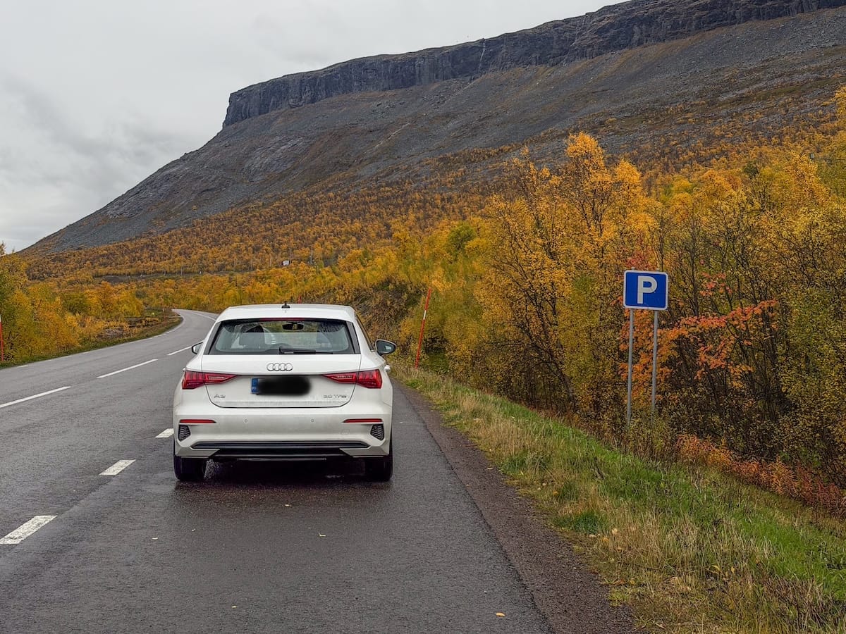 a white audi car parked on a roadside under an autumn mountain