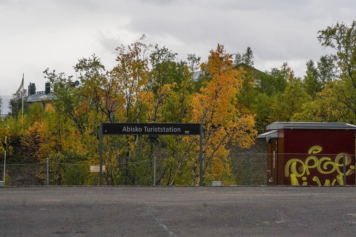 a sign for Abisko Turiststation platform in sweden under autumnal trees