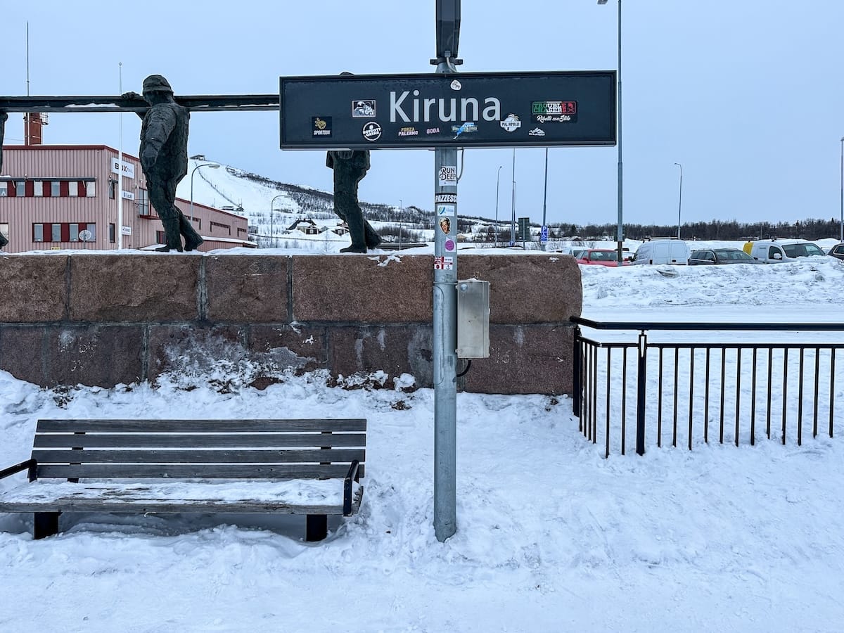 A sign at a train station that says Kiruna; the background is snowy
