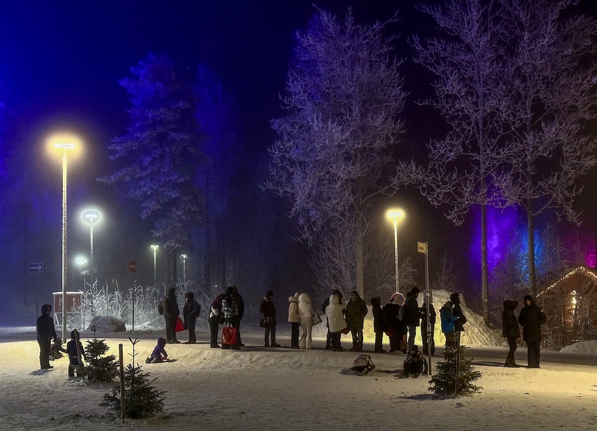 people queuing for a bus at santa claus village in dark skies and snow