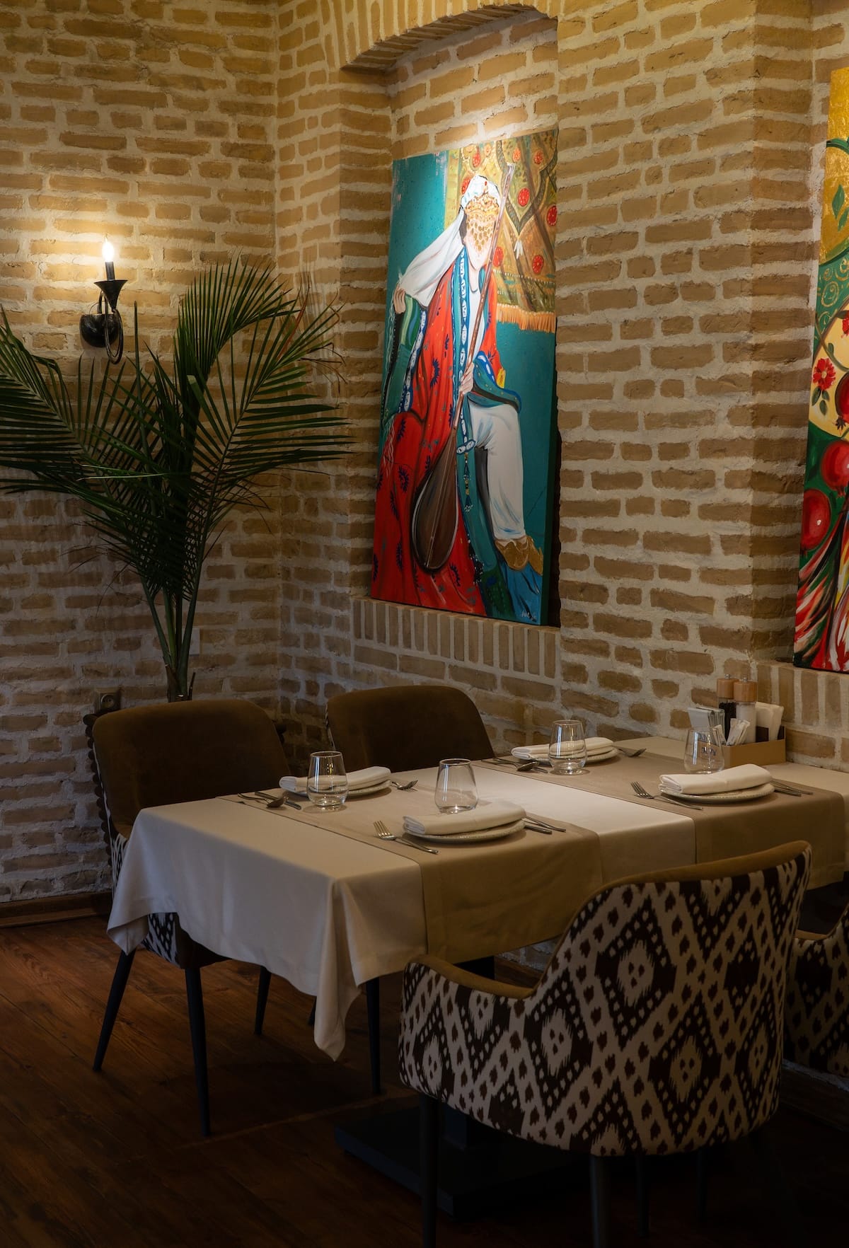 Elegant dining table with traditional artwork on brick wall inside Joy Restaurant in Bukhara, Uzbekistan