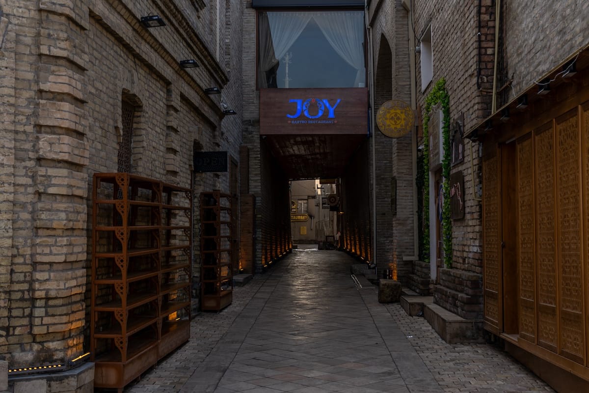 Illuminated alleyway entrance leading to Joy Restaurant in Bukhara, Uzbekistan
