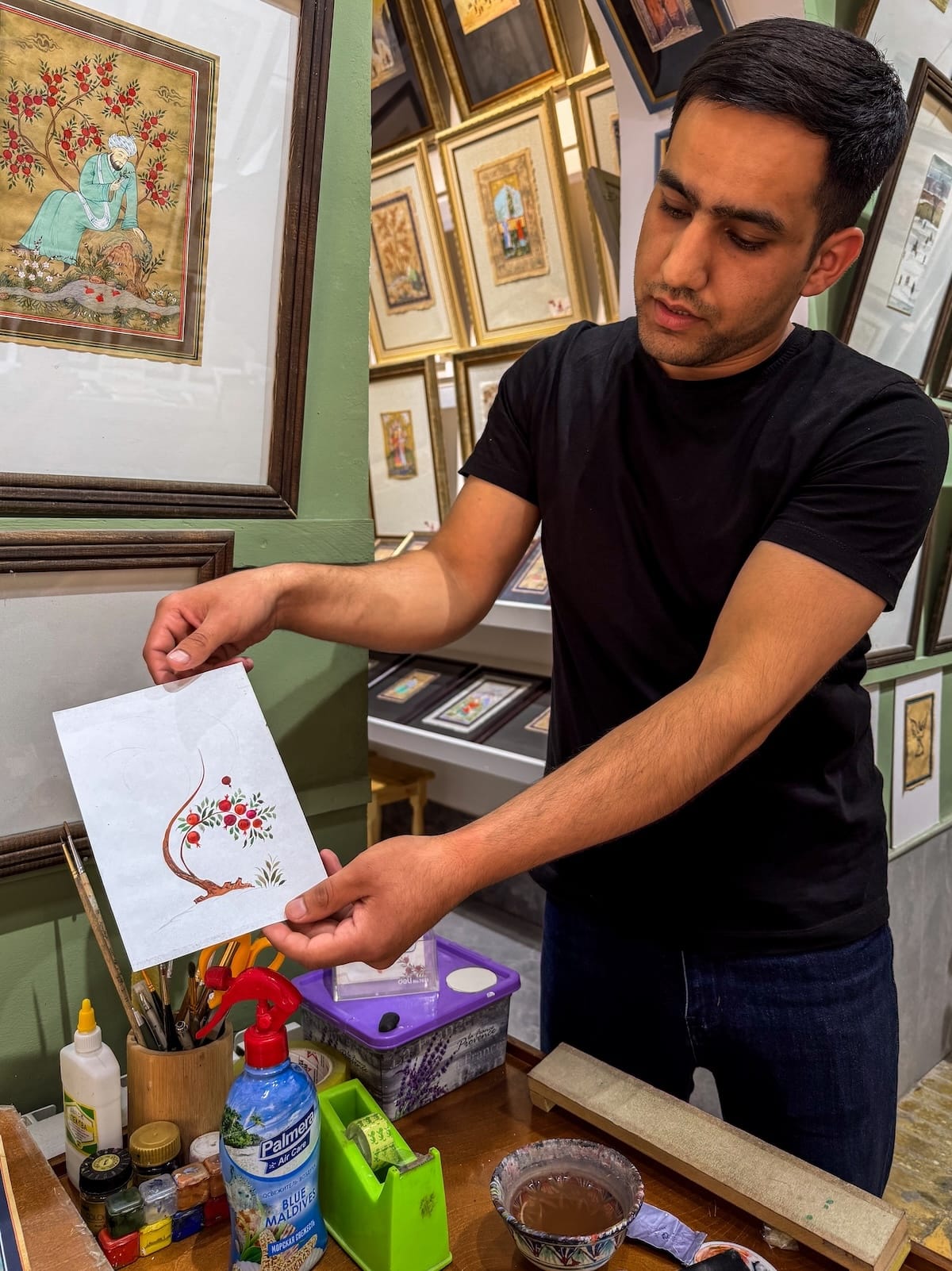 a man holding up a miniature painting in a workshop in uzbekistan
