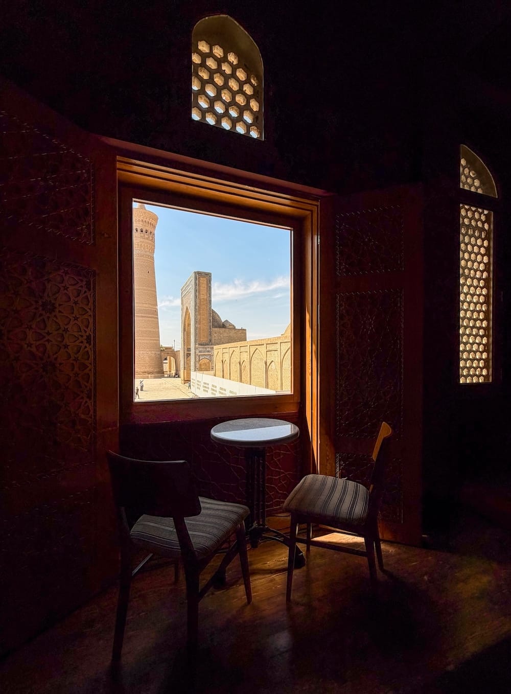 Pavillon Kalan's cafe
two chairs and a table beside a window overlooking a mosque in uzbekistan