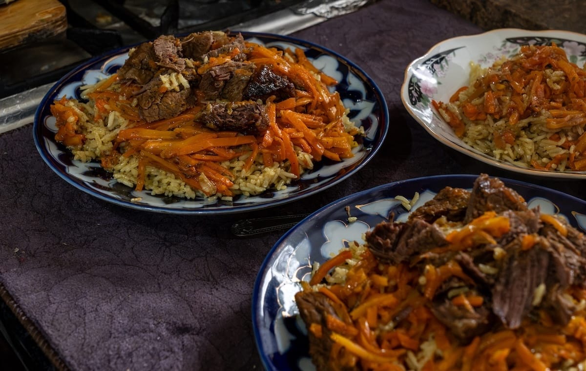 Freshly made plov with beef and carrots served on traditional plates during a home cooking class in Bukhara, Uzbekistan