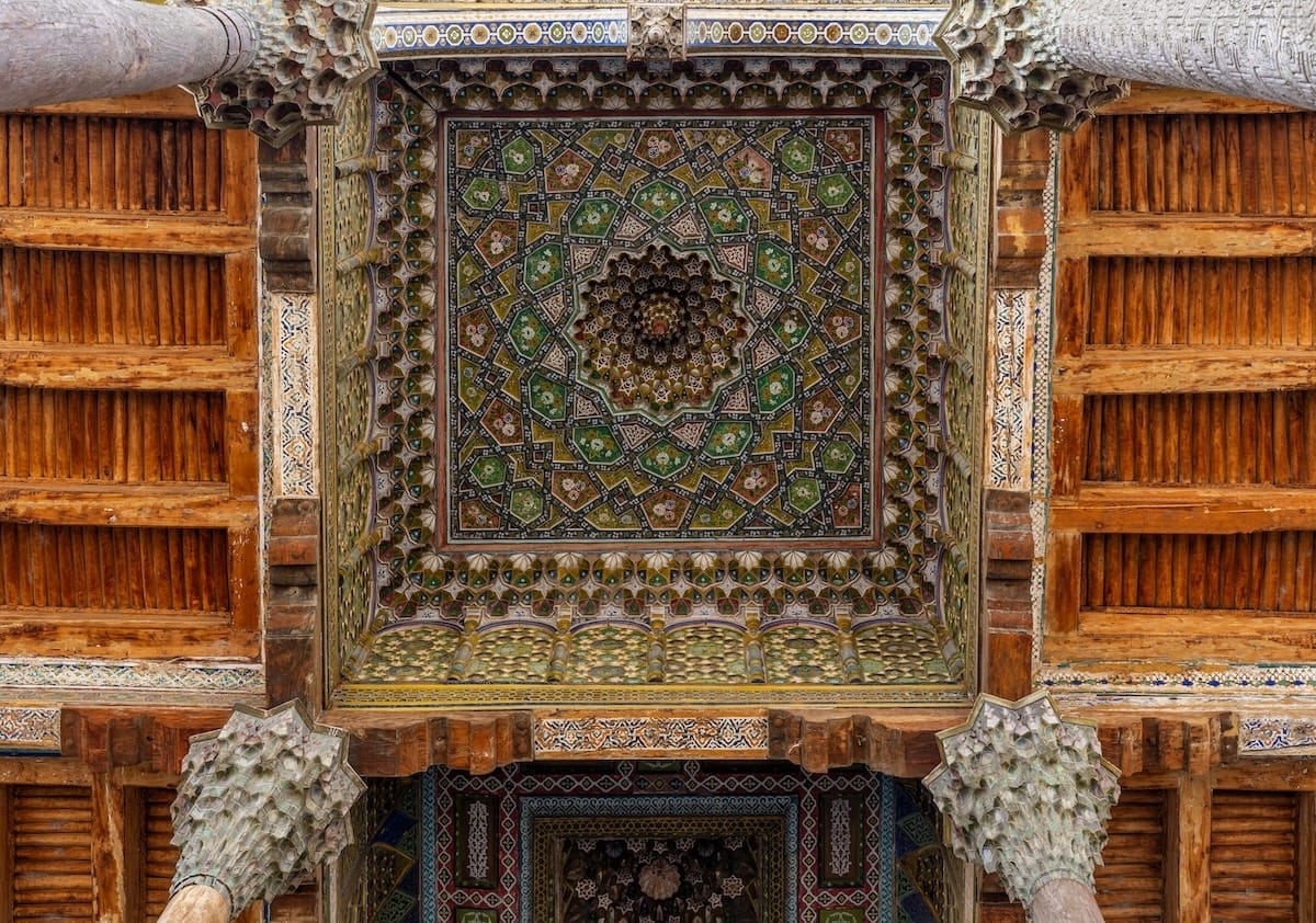 Ornately painted geometric ceiling and carved wooden columns at Bolo Hauz Mosque in Bukhara, Uzbekistan