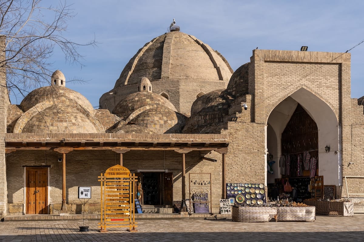 Bukhara in winter

Brick trading dome in Bukhara’s old town with a stork nest on top, a pointed arch entrance, a tea house sign, and stalls selling ceramics and textiles