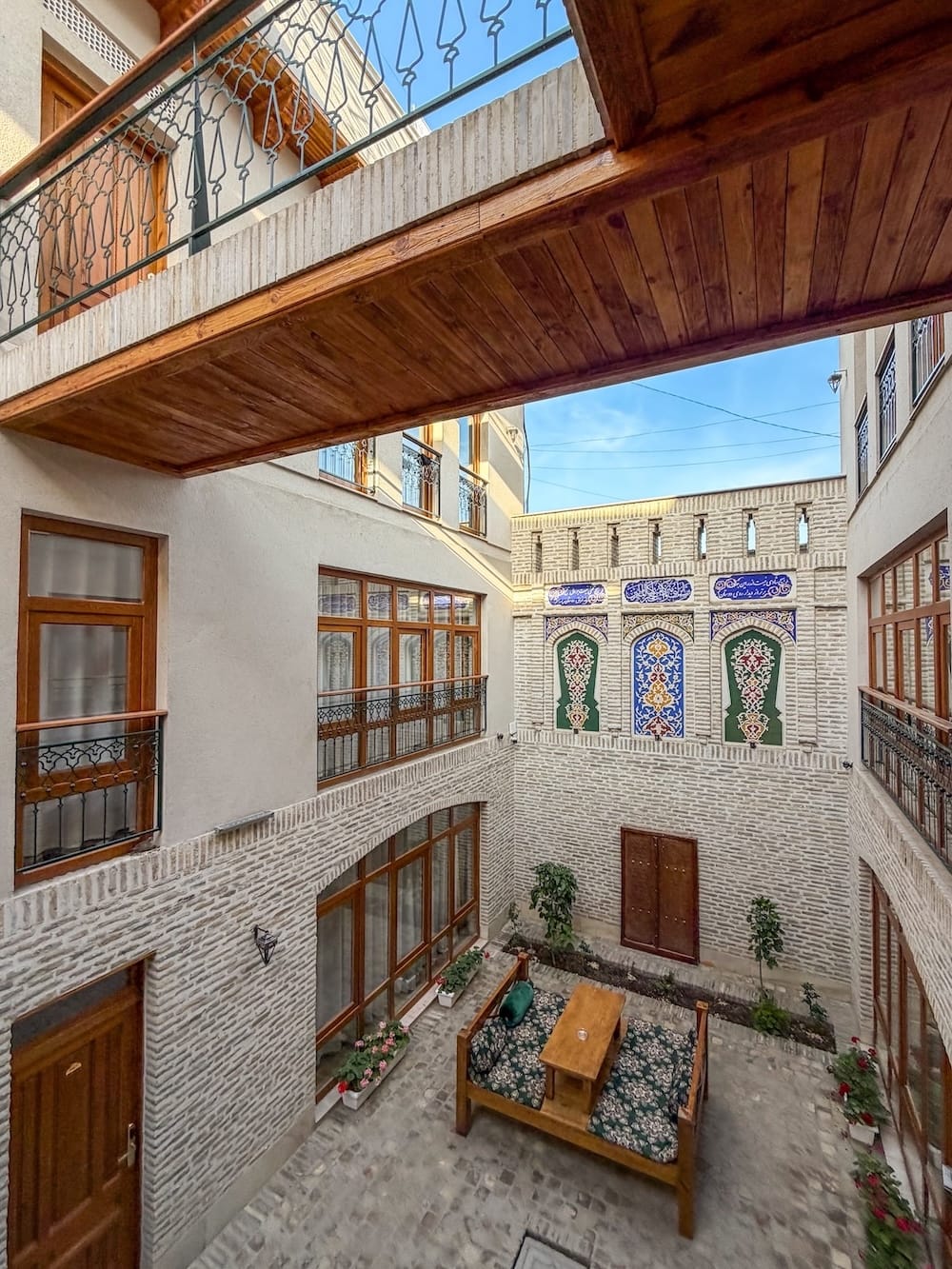 View down into the brick courtyard with painted wall panels and seating at Duston Boutique Hotel in Bukhara, Uzbekistan