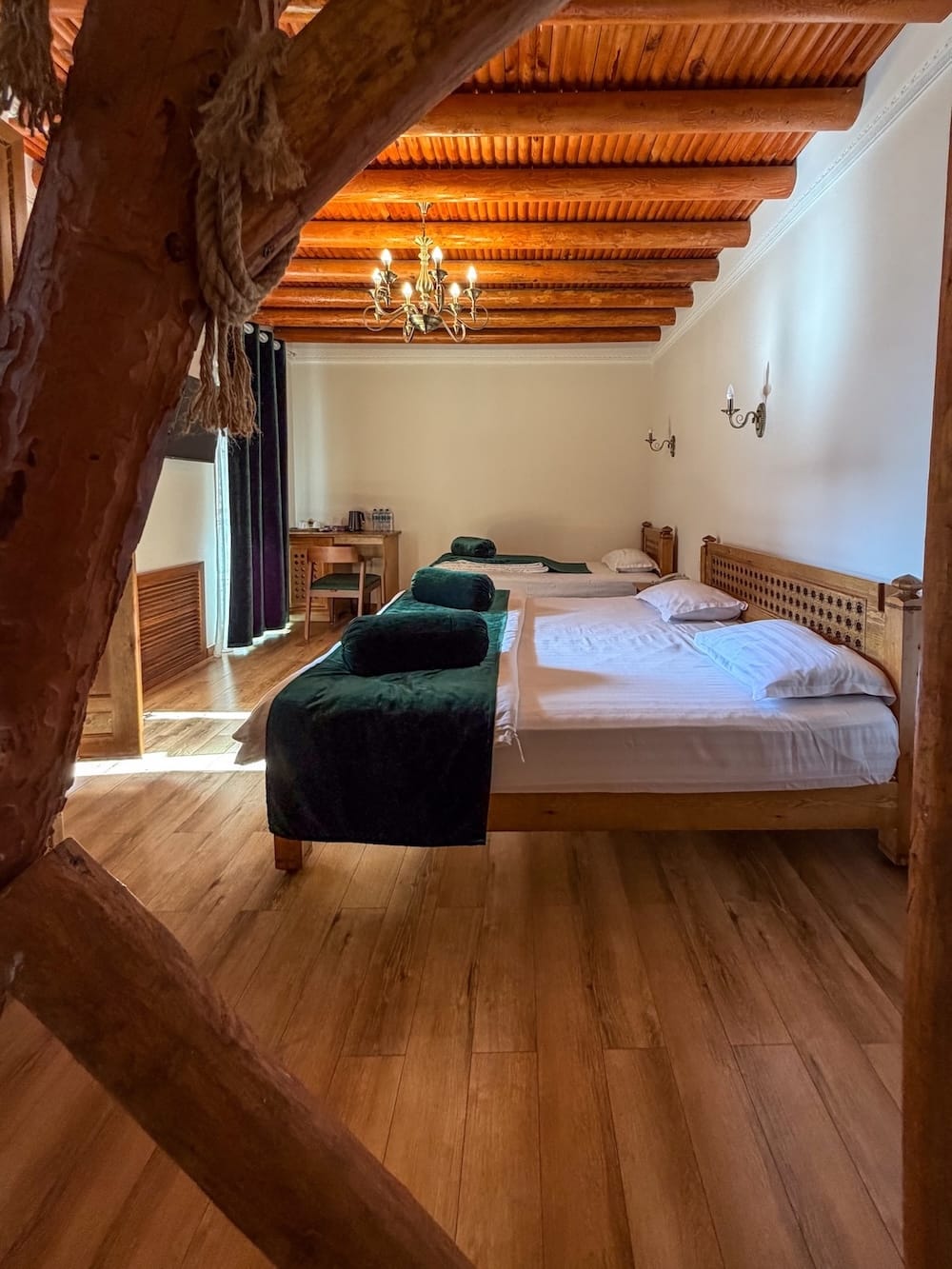 Guest room with exposed wooden ceiling beams, chandelier, and twin beds at Duston Boutique Hotel in Bukhara, Uzbekistan