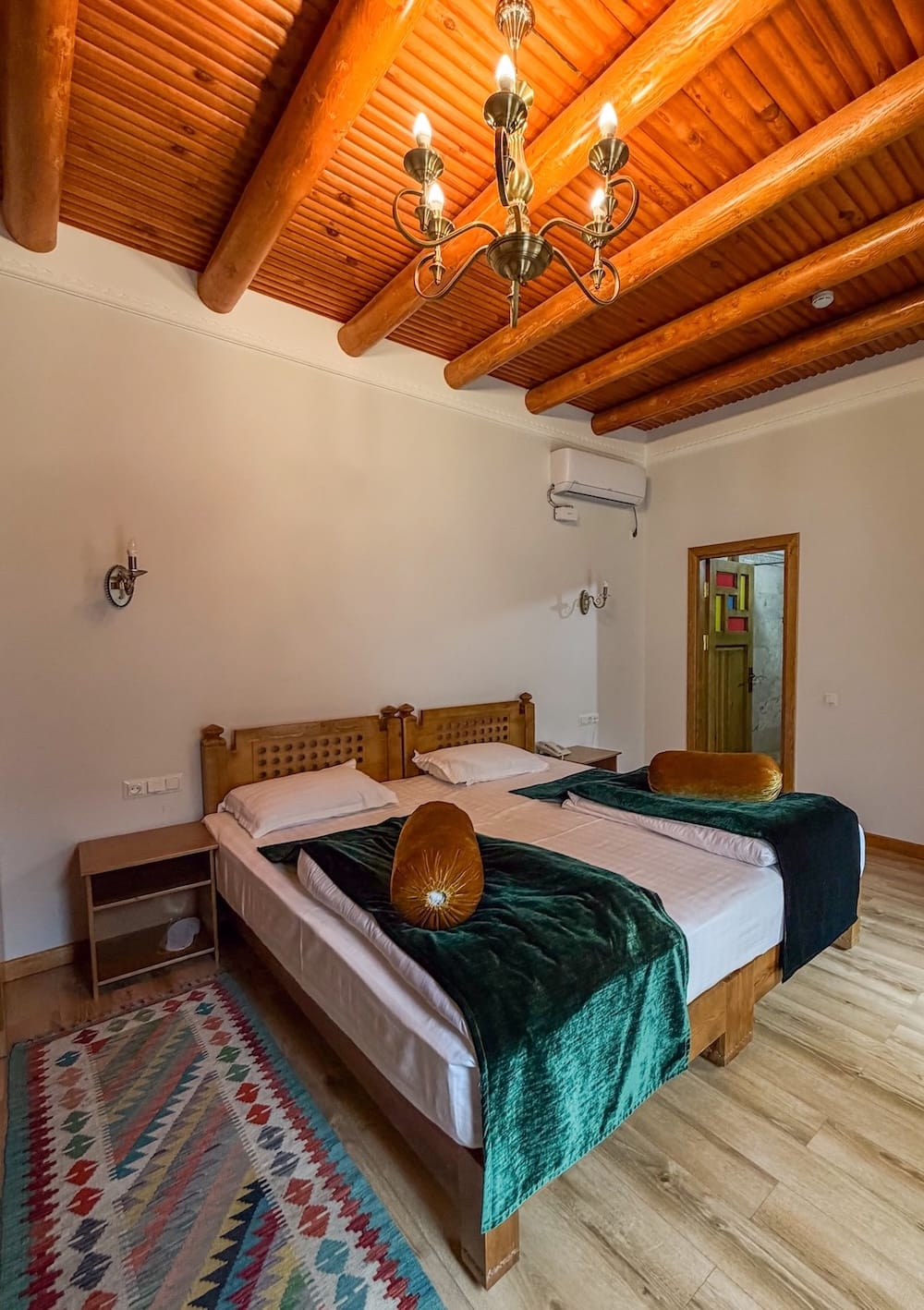 Guest room with a double bed, green velvet throw, and wooden beam ceiling at Duston Boutique Hotel in Bukhara, Uzbekistan