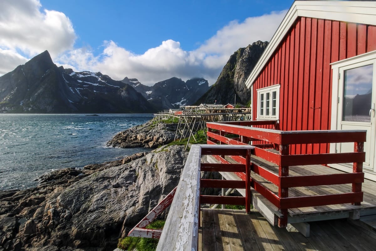 Red rorbu cabin with a wooden deck overlooking the fjord, rocky shore and mountains at Eliassen Rorbuer in Hamnøy, Lofoten