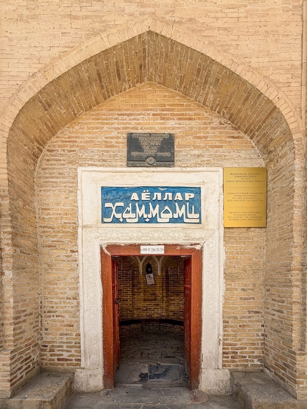 Entrance to the historic Kunjak women's hammam with a brick archway and blue sign in Bukhara, Uzbekistan