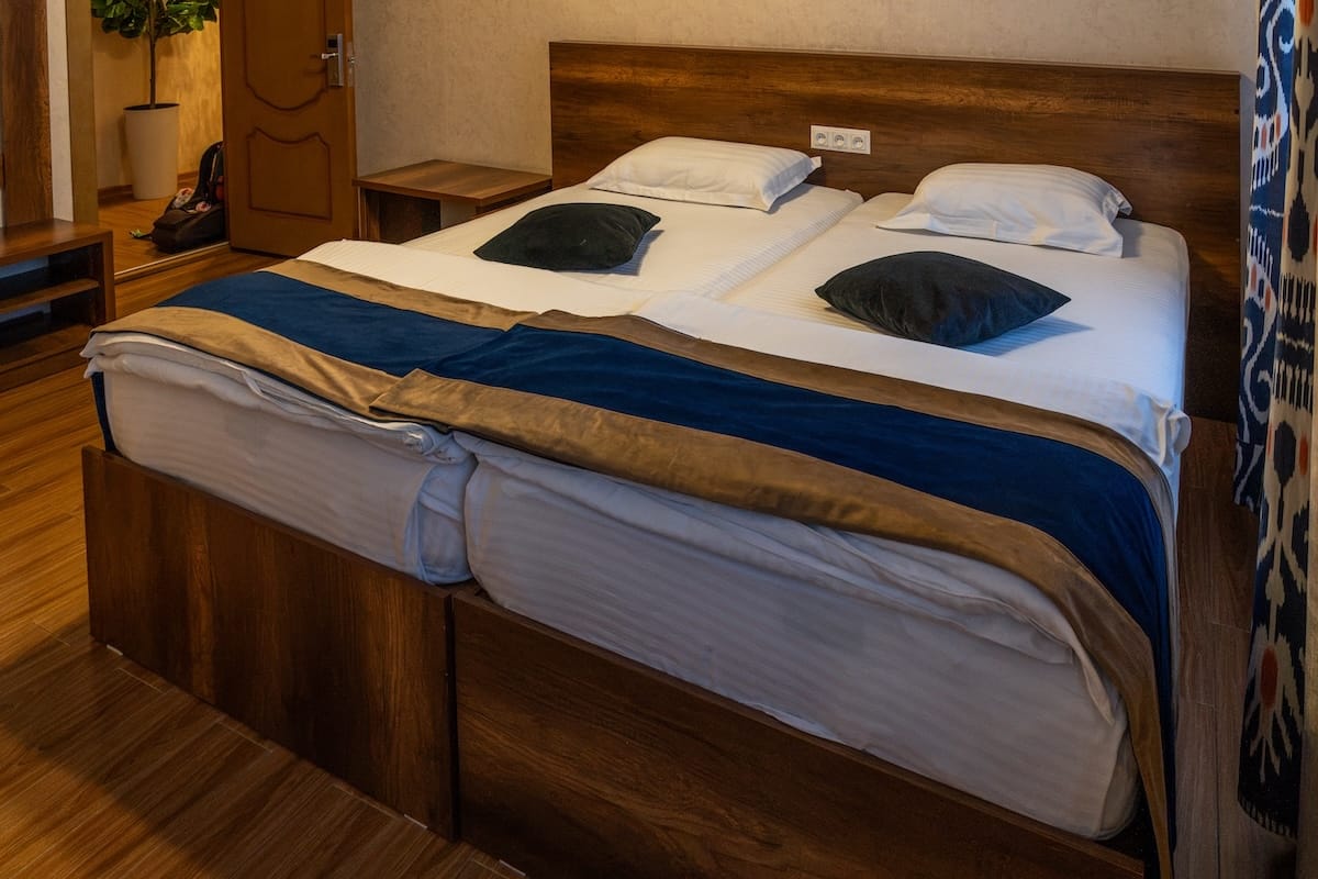 Guest room with a double bed, blue velvet runner, and ikat curtain at Hotel Rayhon in Bukhara, Uzbekistan