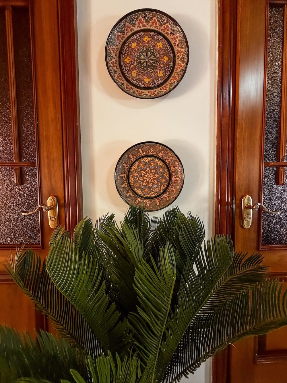 Painted ceramic wall plates between wooden doors above a green plant at Hotel Rayhon in Bukhara, Uzbekistan