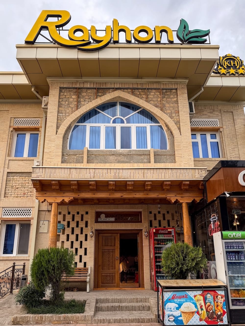 Brick facade with carved wooden entrance and yellow sign at Hotel Rayhon in Bukhara, Uzbekistan