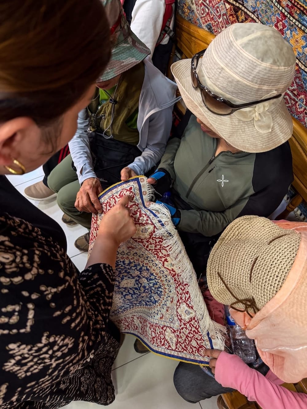 Learning about carpet weaving with Dilnoza in Bukhara
Visitors in sun hats gather around a guide pointing out the fine knotting on a small hand-knotted silk carpet at a carpet workshop in Bukhara