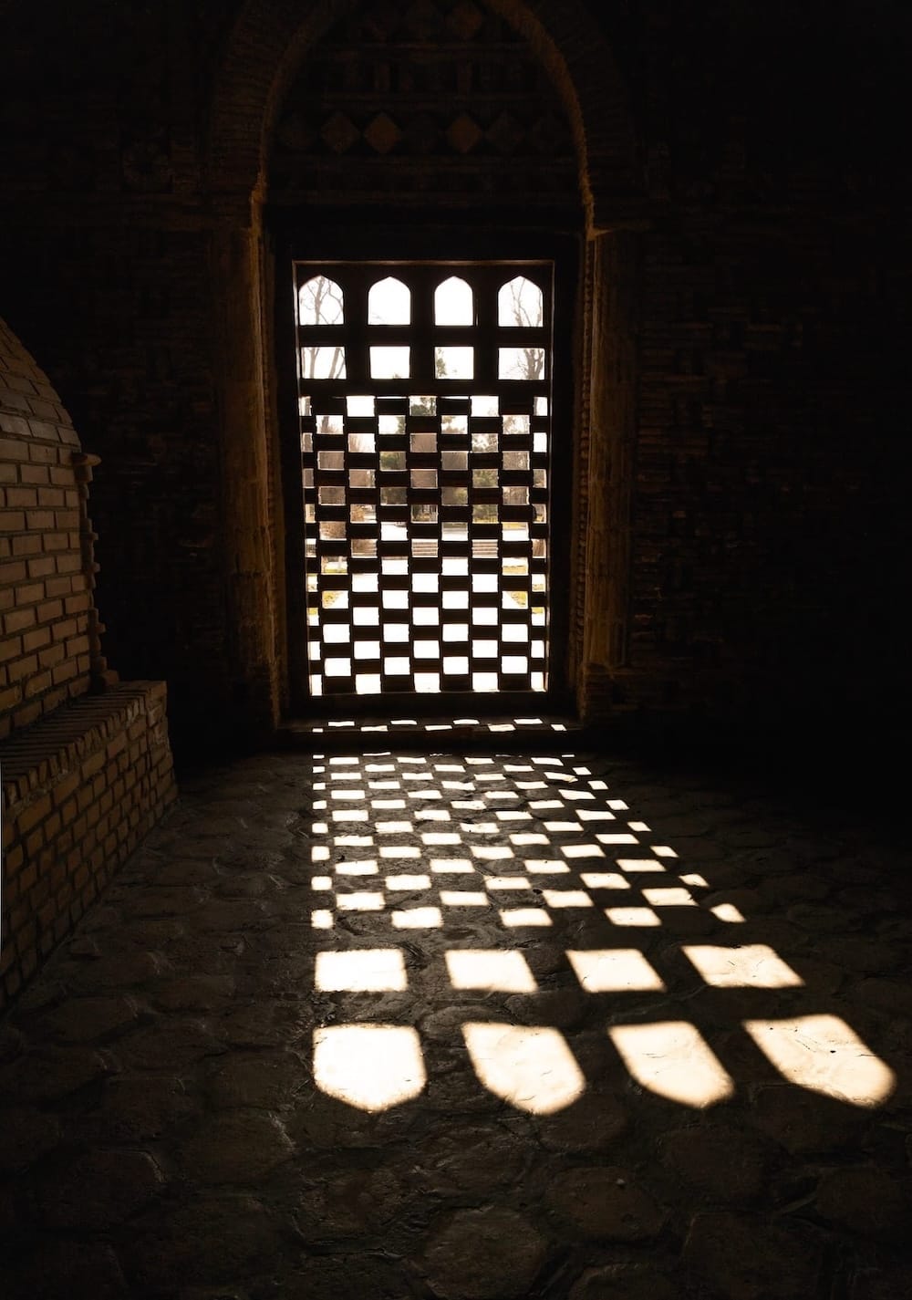 Latticed window casting checkered light patterns inside the Ismail Samani Mausoleum in Bukhara, Uzbekistan