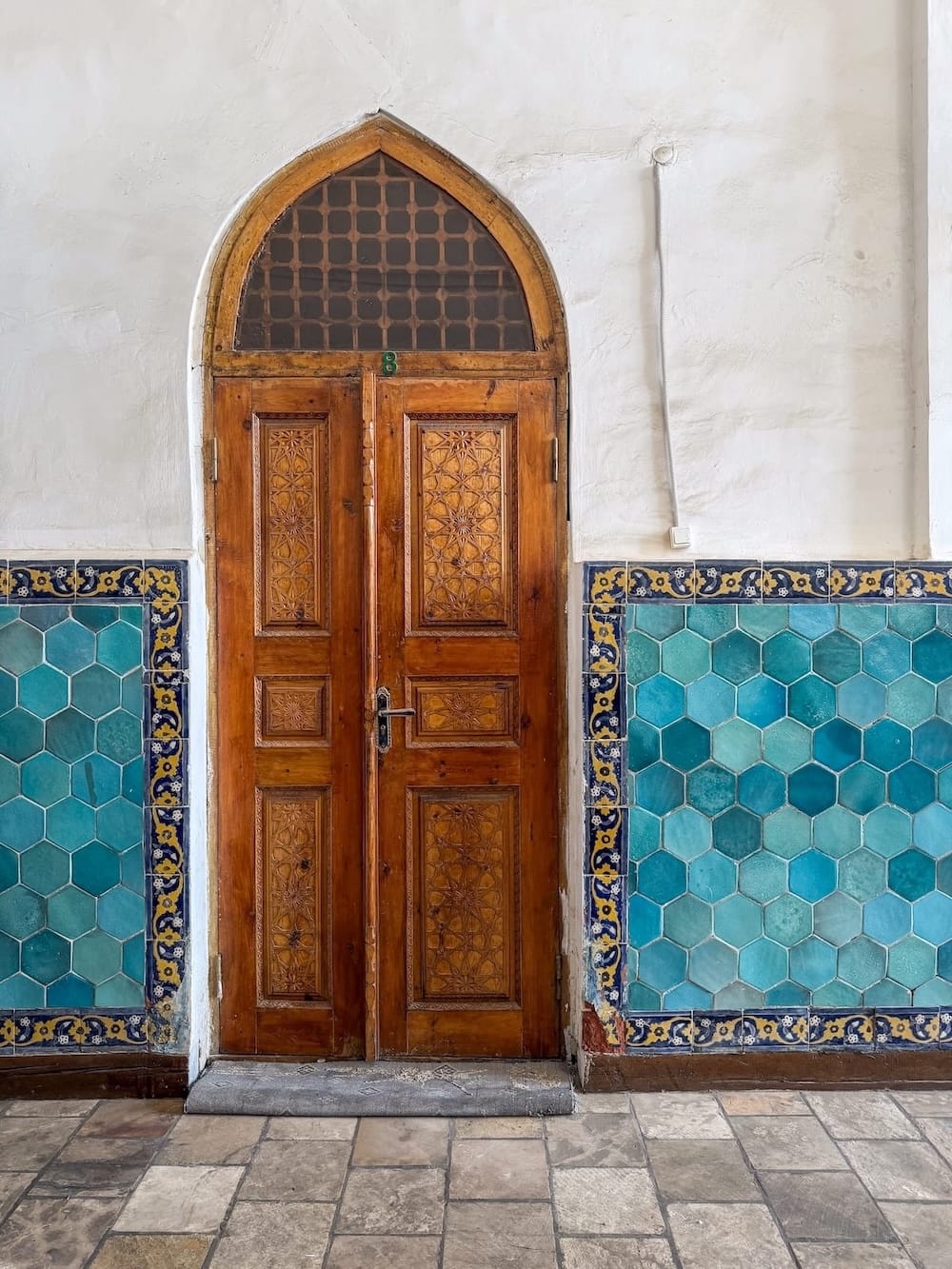 Carved wooden door framed by turquoise hexagonal tiles at Kalyan Mosque in Bukhara, Uzbekistan