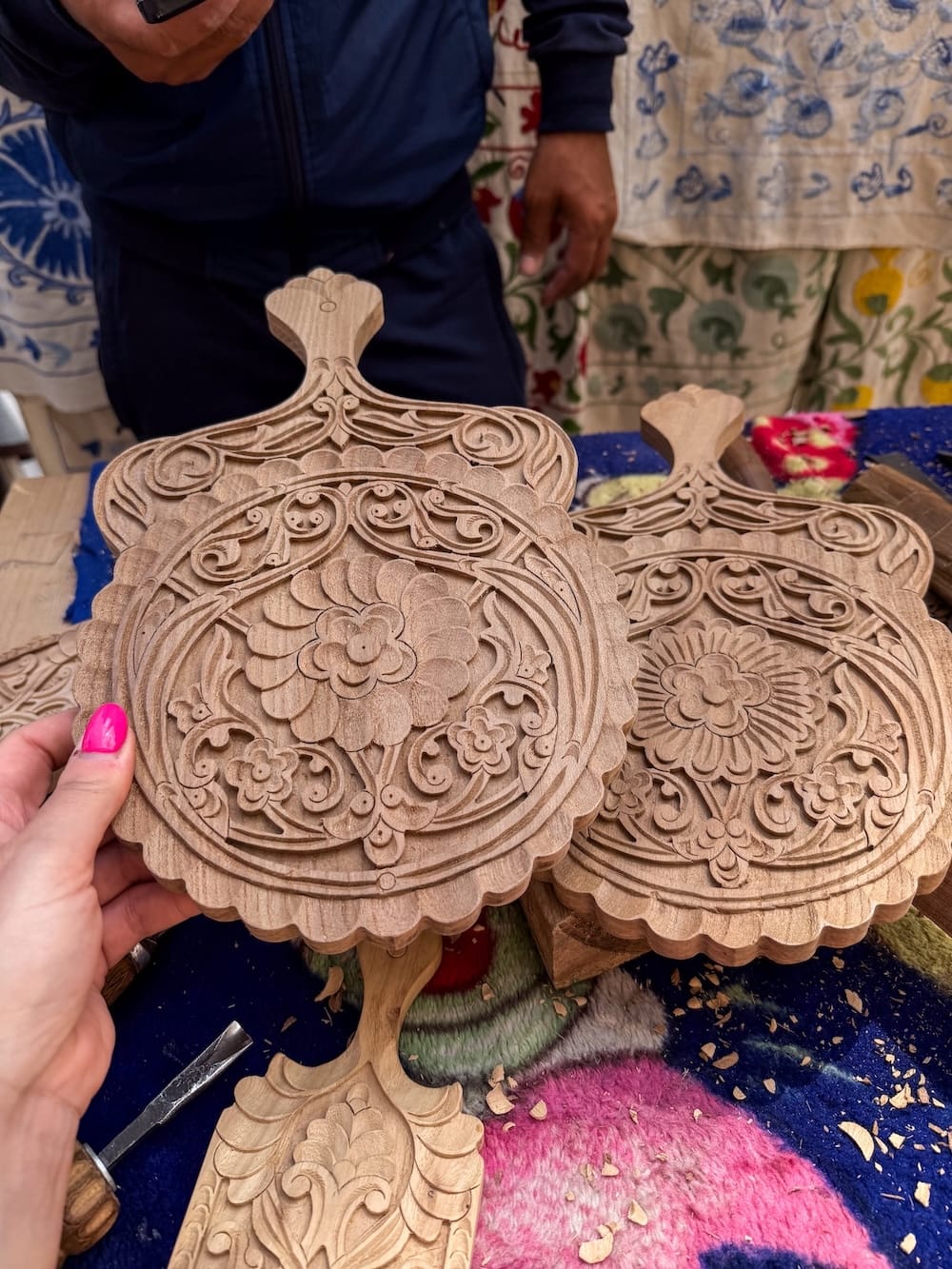 Hand-carved wooden boards with floral and scrollwork patterns on a table with carving chisels and wood shavings at a woodcarving workshop in Khiva