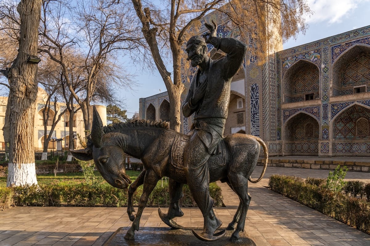 Bronze statue of Nasreddin Hodja riding a donkey in Lyabi-Hauz, with the tiled facade of the Nadir Divan-Begi Madrasa and bare trees behind it