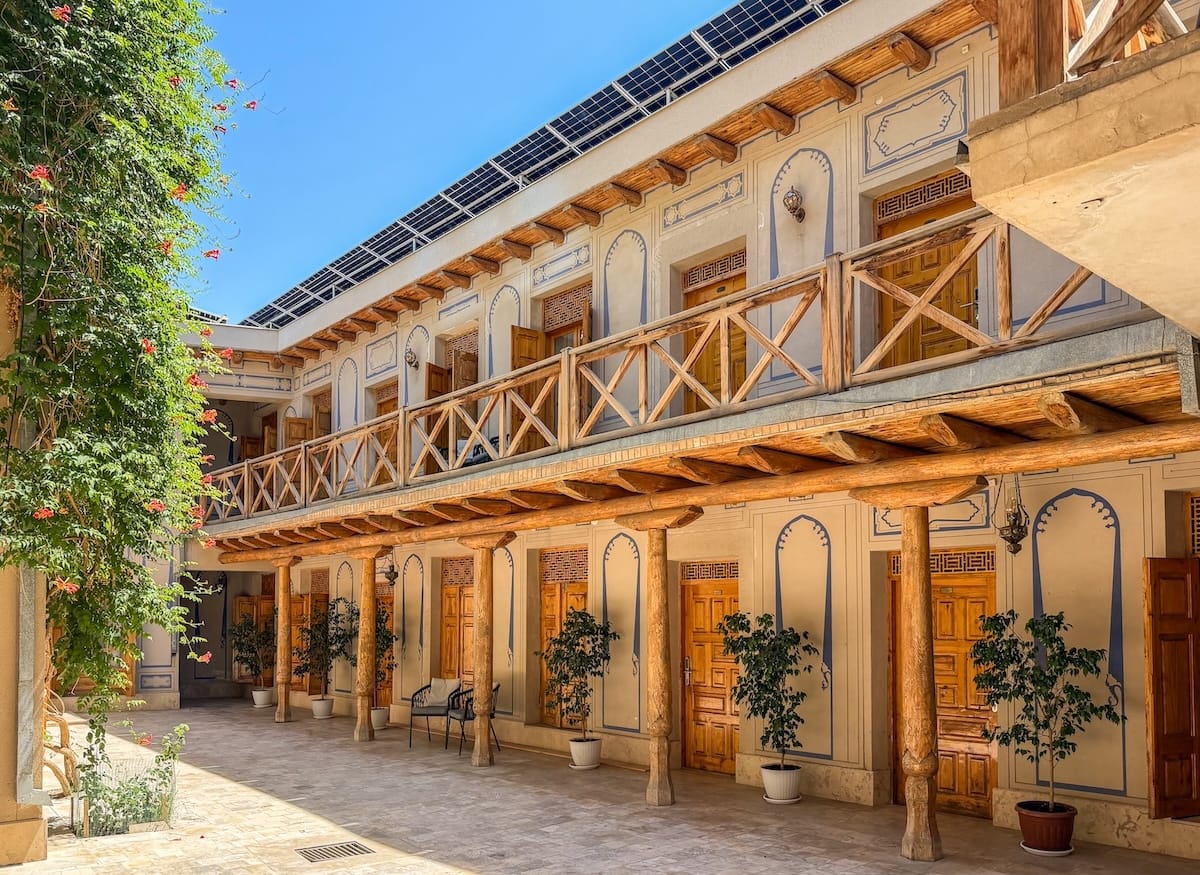 Sunny courtyard with wooden columns, carved doors, and balcony at Lyabi House Hotel in Bukhara, Uzbekistan