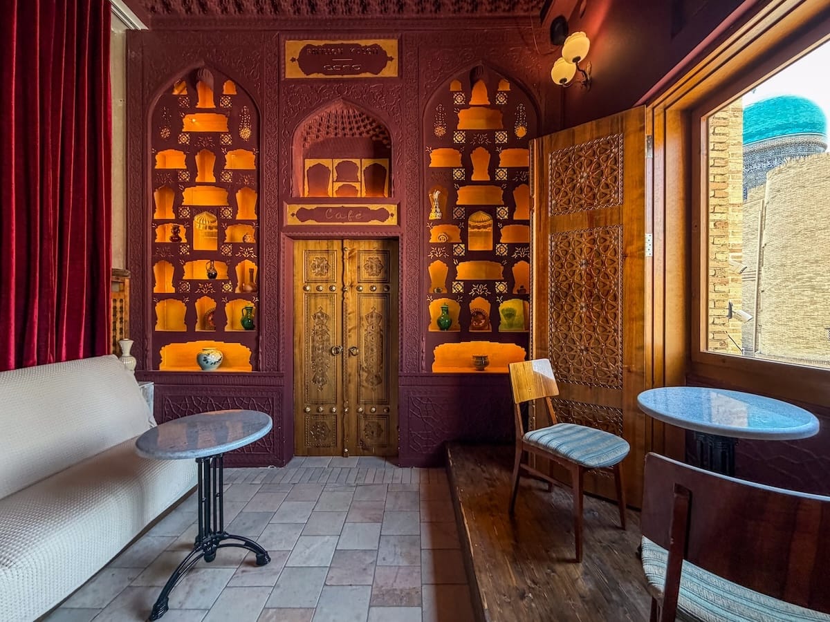 Cozy maroon-toned cafe interior with carved wooden door and minaret view at Pavillon Kalon in Bukhara, Uzbekistan