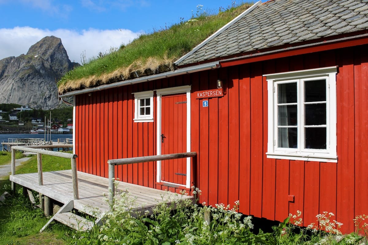 Red rorbu cabin with a grass-covered roof and wooden deck at Reine Rorbuer by Classic Hotels in Reine, Lofoten