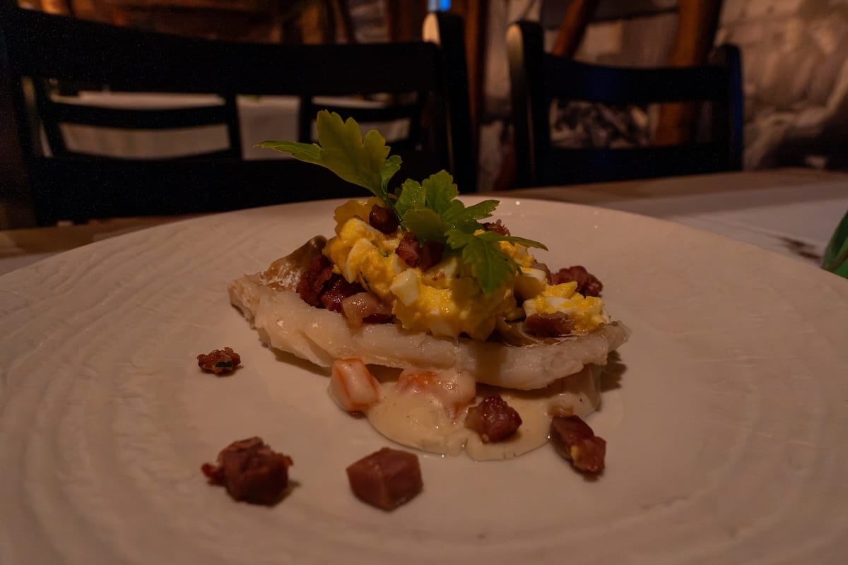 Plated cod dish topped with egg, bacon pieces and herbs at a restaurant in Svolvær