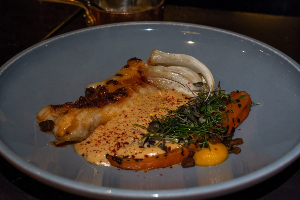 Grilled white fish with roasted fennel, carrot and a creamy sauce topped with microgreens at a restaurant in Svolvær