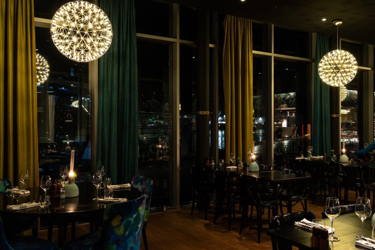 Restaurant dining room in Svolvær with globe pendant lights, green and mustard velvet curtains and harbor views at night