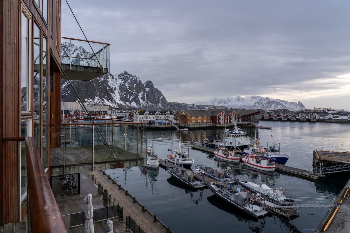 View from a balcony over the Svolvær marina, with snow-covered mountains and red rorbu cabins