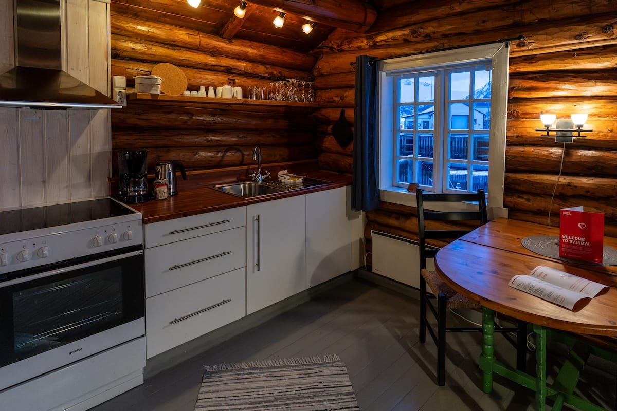 Log cabin kitchen on Svinøya in Svolvær with a wooden table and a window overlooking the harbor Where to stay in Svolvær