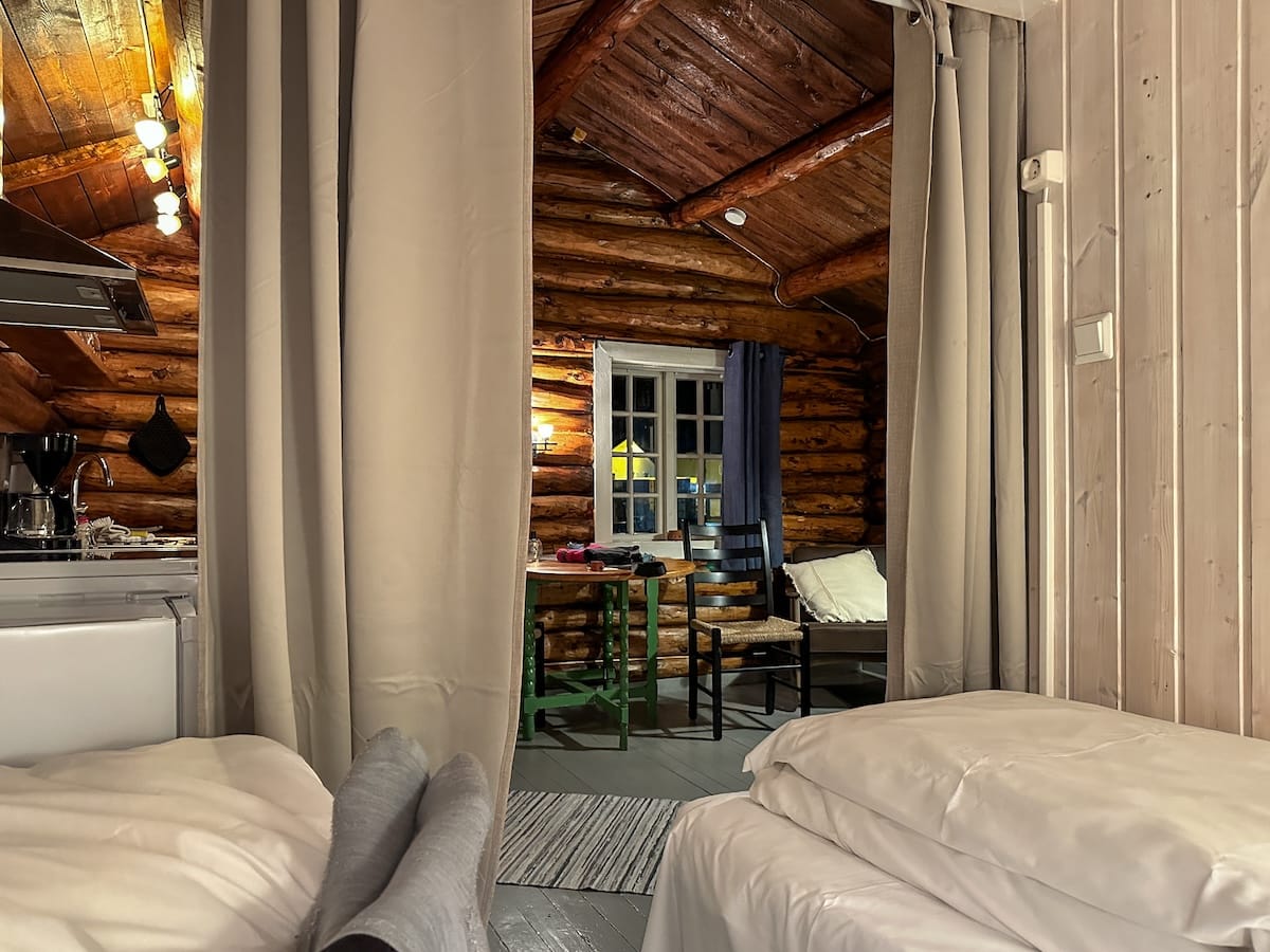 Cozy log cabin interior on Svinøya, Svolvær, seen from the bed, with a green wooden table and exposed beams