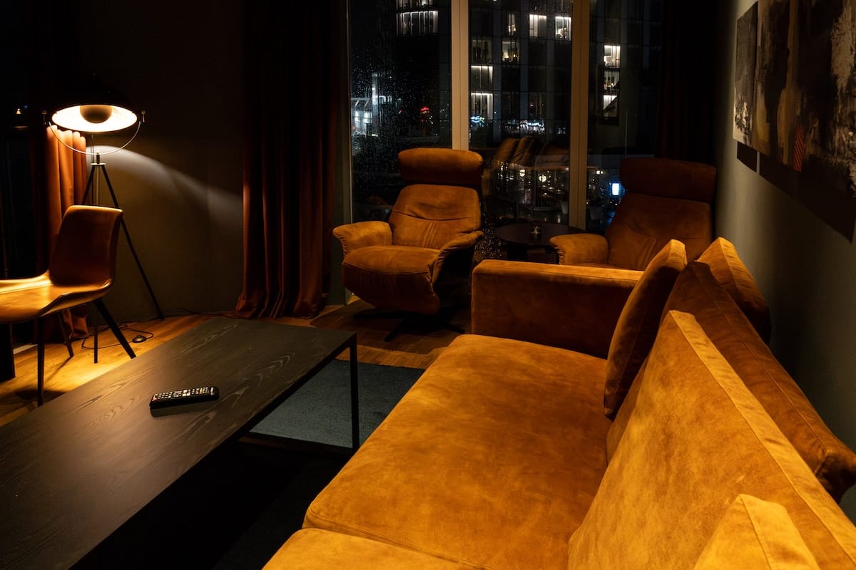 Living area at Nordis Apartments with a mustard velvet sofa, two matching armchairs and floor-to-ceiling windows overlooking the city at night